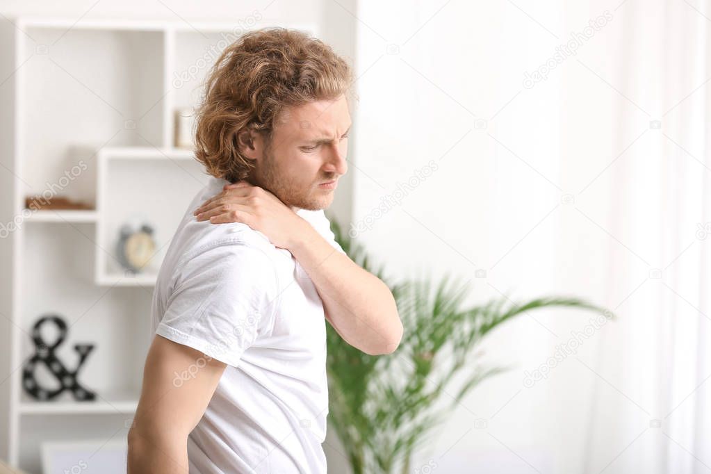 Young man suffering from pain in shoulder at home