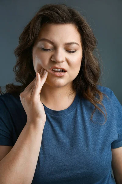 Плюс розмір жінки, яка страждає від зубного болю на сірому фоні — стокове фото