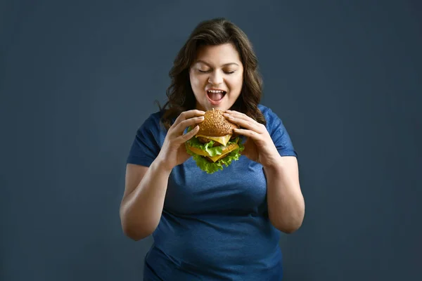 Além de mulher tamanho com hambúrguer saboroso no fundo cinza. Conceito de corpo positivo — Fotografia de Stock