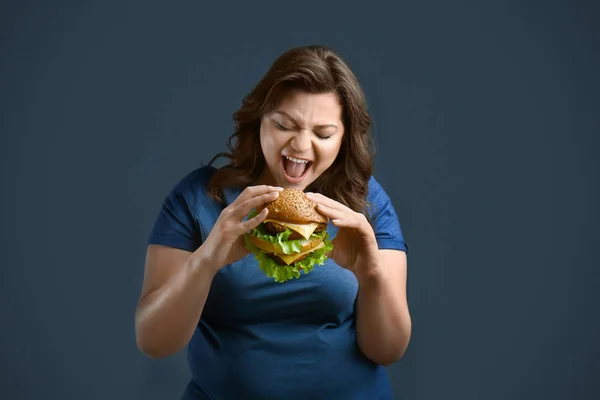 Plus Size vrouw met smakelijke Hamburger op grijze achtergrond. Concept van lichaam positief — Stockfoto