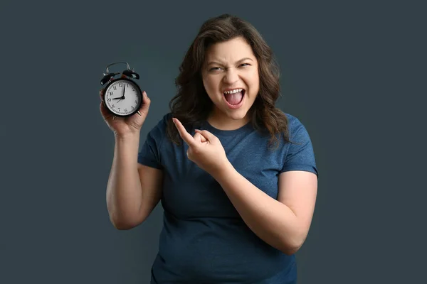 Irritated plus size woman with alarm clock on grey background — Stock Photo, Image