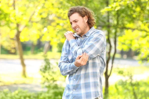 Young man suffering from pain in elbow outdoors — Stock Photo, Image