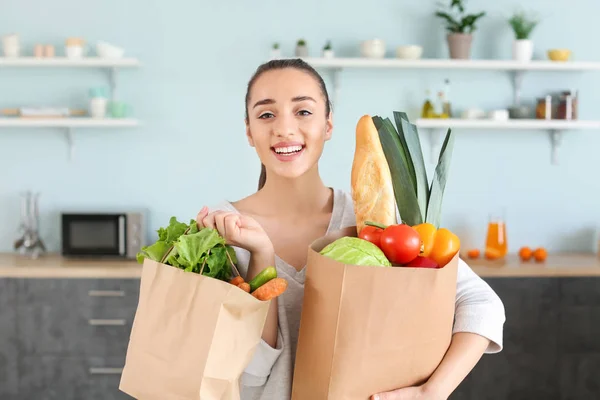 Beautiful woman with shopping bags full of fresh products in kitchen at home — Stock Photo, Image