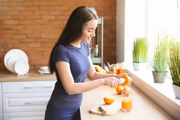 Smuk kvinde forbereder appelsinjuice i køkkenet derhjemme - Stock-foto