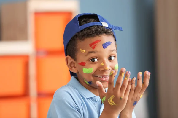 Cute African-American boy with hands and face in paint at home — Stock Photo, Image