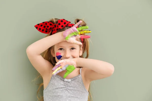 Cute little girl with hands and face in paint on color background — Stock Photo, Image