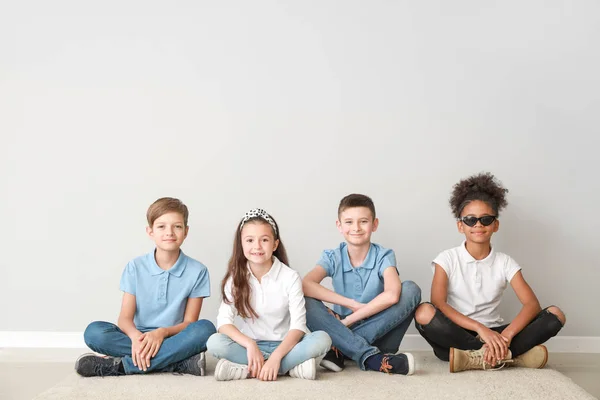 Niños con estilo en jeans sentados cerca de la pared de luz —  Fotos de Stock