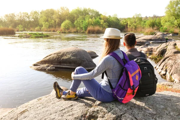 Пара молодых туристов, сидящих на скале возле реки — стоковое фото