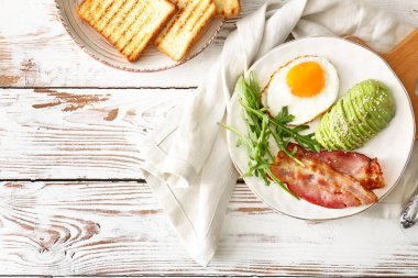 Ahşap masada lezzetli kızarmış yumurta, avokado ve pastırma ile Tabak