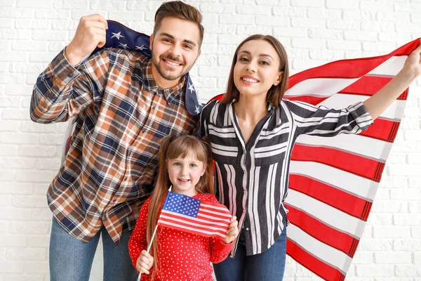 Glückliche junge Familie mit US-Nationalflaggen in der Nähe der weißen Backsteinmauer — Stockfoto