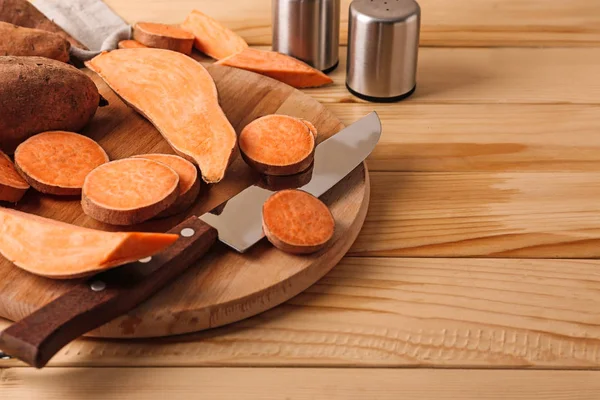 Cutting board and knife with raw sweet potato on wooden background