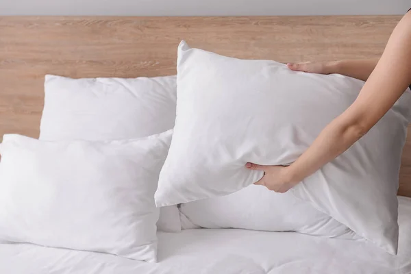 Woman fluffing soft pillows on bed — Stock Photo, Image