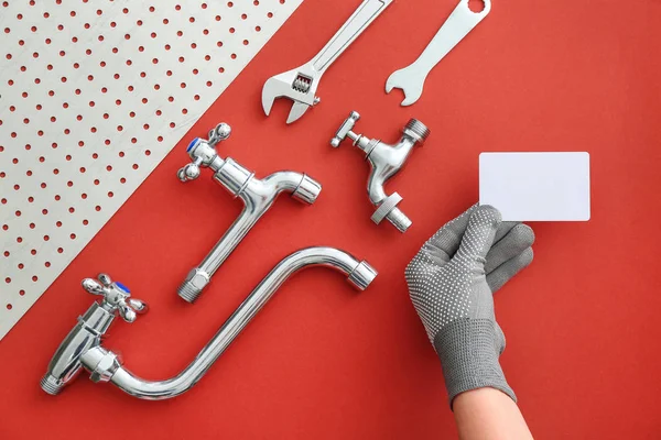 Hand of plumber with business card and items on color background — Stock Photo, Image