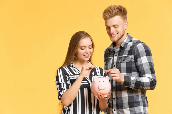 Pareja feliz poniendo monedas en alcancía en el fondo de color —  Fotos de Stock