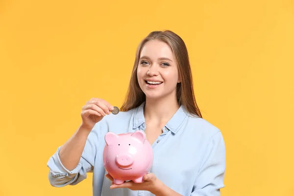 Mujer joven poniendo moneda en alcancía en el fondo de color —  Fotos de Stock