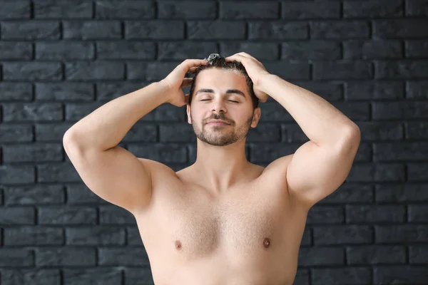 Handsome man washing hair on dark background — Stock Photo, Image