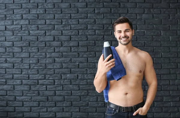 Schöner Mann mit einer Flasche Shampoo und Handtuch auf dunklem Hintergrund — Stockfoto