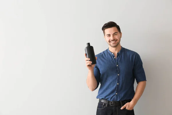 Handsome man with bottle of shampoo on light background — Stock Photo, Image