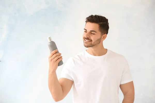 Handsome man with bottle of shampoo on light background — Stock Photo, Image