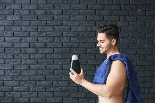 Hombre guapo con botella de champú y toalla sobre fondo oscuro — Foto de Stock