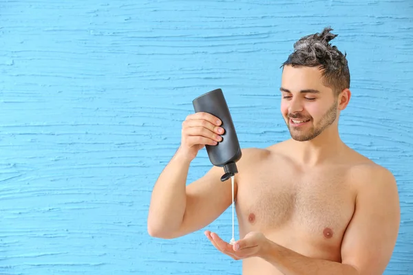 Bel homme avec bouteille de shampooing sur fond de couleur — Photo