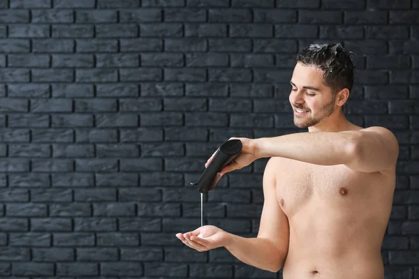 Hombre guapo con botella de champú sobre fondo oscuro — Foto de Stock