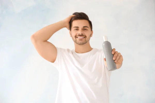 Handsome man with bottle of shampoo on light background — Stock Photo, Image