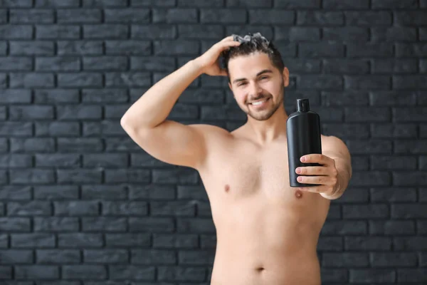 Handsome man with bottle of shampoo on dark background — Stock Photo, Image