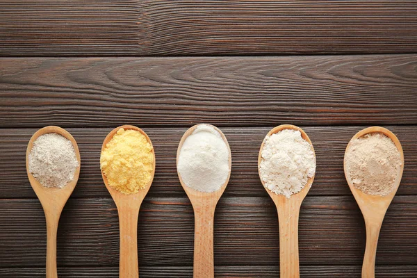 Spoons with different kinds of flour on wooden background — Stock Photo, Image