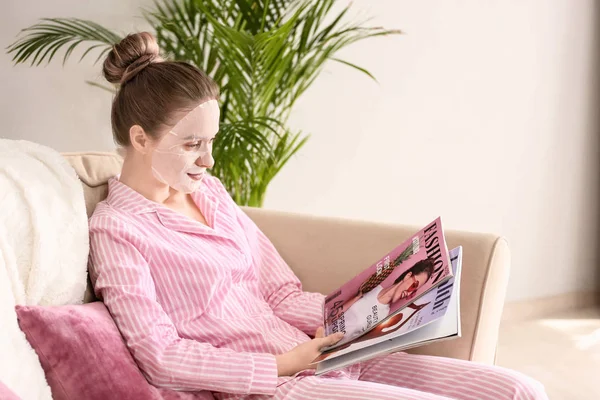 Ung kvinna med blad ansiktsmask läsning Magazine hemma — Stockfoto