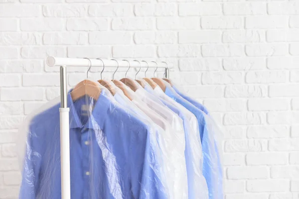 Rek met kleren na drogen-reiniging in de buurt van witte bakstenen muur — Stockfoto