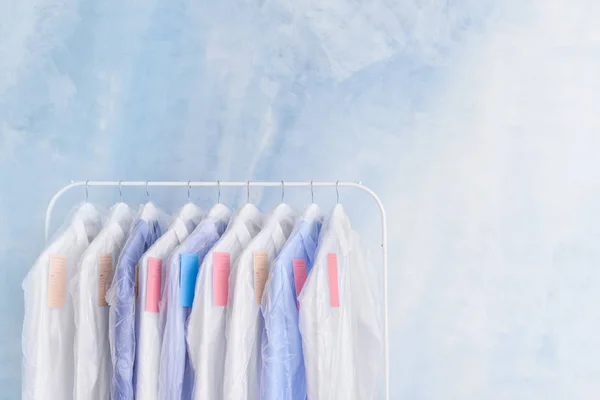 Scaffale con vestiti dopo lavaggio a secco su sfondo chiaro — Foto Stock