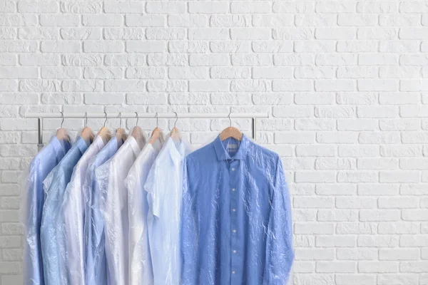 Rack with clothes after dry-cleaning near white brick wall — Stock Photo, Image