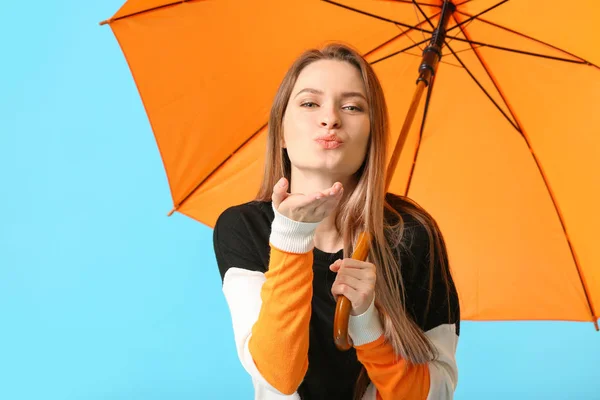 Beautiful young woman with umbrella blowing kiss on color background — Stock Photo, Image