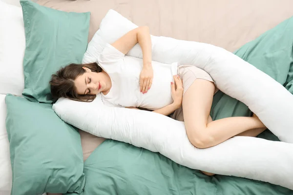 Молодая беременная женщина спит на подушке для беременных дома — стоковое фото