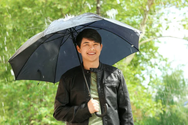 Pohledný asijský muž s deštníkem venku v deštivém dni — Stock fotografie
