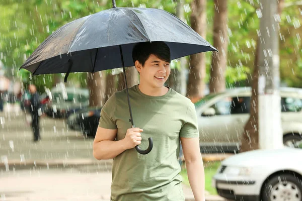 Pohledný asijský muž s deštníkem venku v deštivém dni — Stock fotografie
