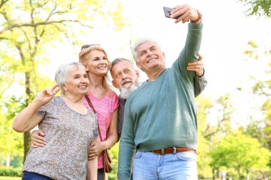 Group of happy senior people taking selfie in park clipart