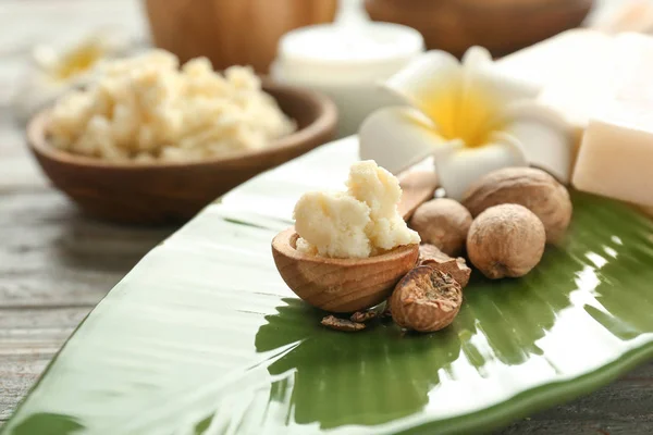 Bowl with shea butter, nuts and flower on plate — Stock Photo, Image