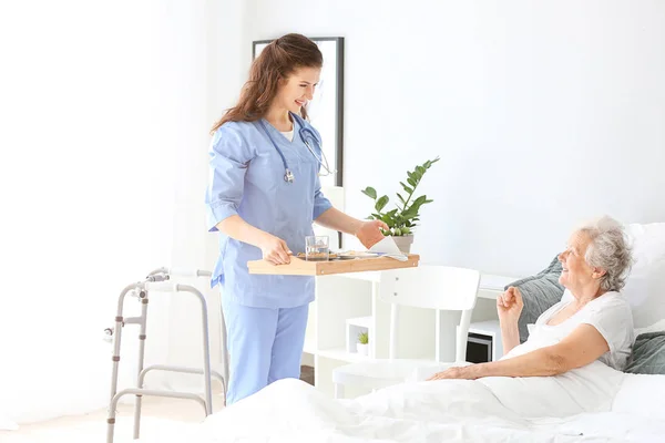 Young caregiver bringing senior woman breakfast in bed — Stock Photo, Image
