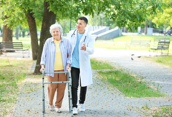 Doctor walking with senior woman in park