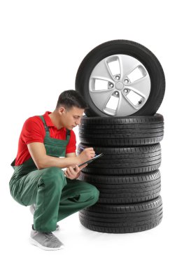 Beyaz arka plan üzerinde araba lastikleri ile üniformalı genç erkek mekanik