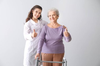 Gri arka planda başparmak-up jest gösteren kıdemli kadın ile genç doktor