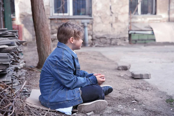 Бездомный маленький мальчик сидит на улице — стоковое фото