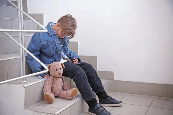 Niño sin hogar con oso de peluche sentado en las escaleras — Foto de Stock