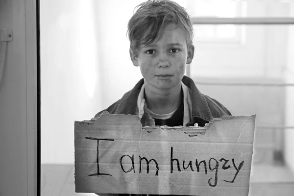 Бездомный мальчик просит еды, смотрит через стеклянную дверь — стоковое фото