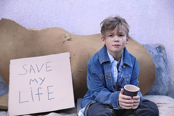 Homeless pequeño niño con taza sentado al aire libre — Foto de Stock