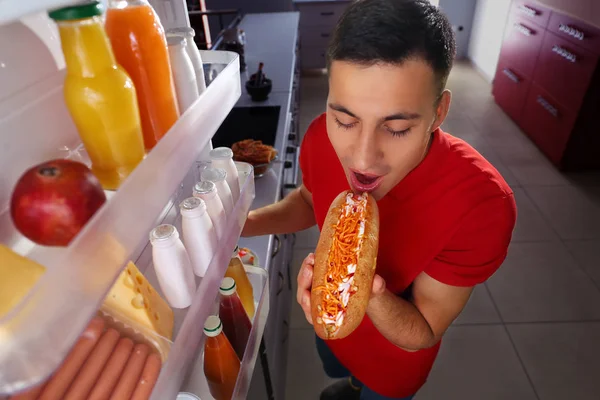 Молодой человек ест еду возле холодильника дома — стоковое фото