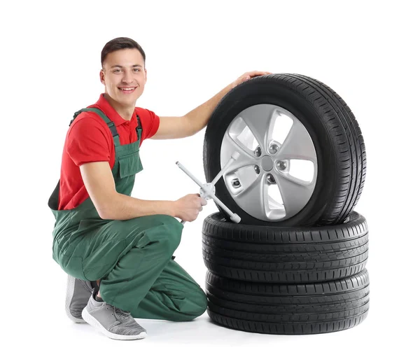 Young male mechanic in uniform with car tires and cross wrench on white background — Stock Photo, Image