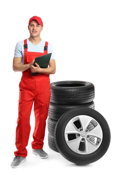 白い背景に車のタイヤと制服を着た若い男性整備士 — ストック写真